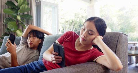 Young couple relaxing on sofa with smartphones at home