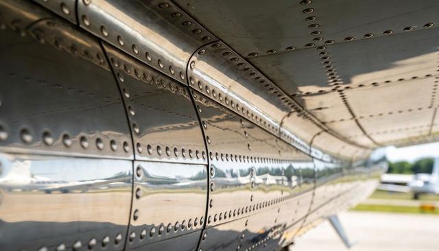Polished riveted aluminum aircraft wing panels reflecting light aircraft on airport ramp