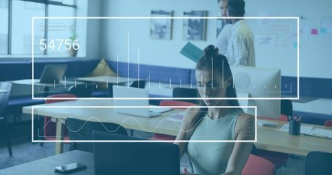 Focused woman typing on laptop in modern coworking space with collaborative team