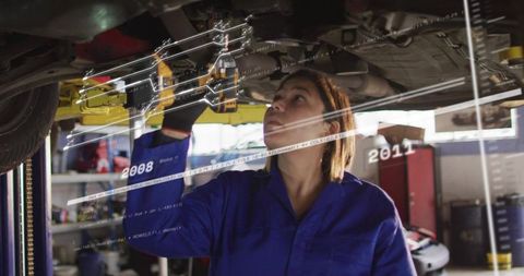 Female mechanic inspecting car undercarriage with ar overlay in busy garage workshop