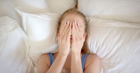 Woman Covering Face with Hands Lying on Bed in Calm Oasis