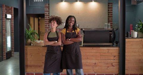 Smiling baristas standing behind rustic cafe counter wearing dark aprons