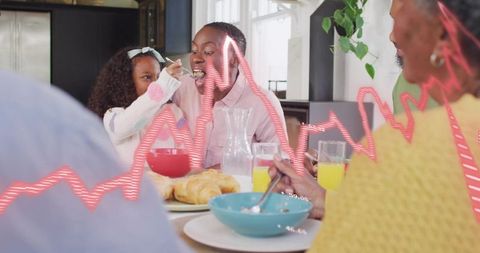 Multigenerational family sharing breakfast as child feeding parent at kitchen table