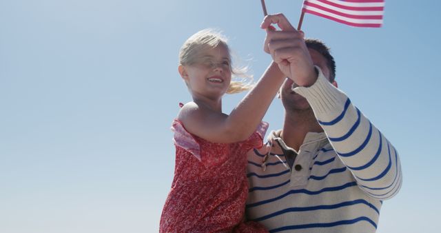 Father and young daughter celebrating outdoors, bonding together while holding an American flag. Bright sunny day enhances the cheerful atmosphere. Ideal for content about family activities, patriotic holidays, Independence Day, parent-child relationships, and outdoor celebrations.