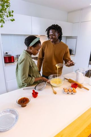 African american couple baking together in modern bright kitchen island mixing batter