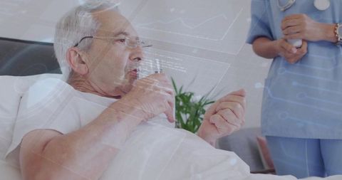 Senior man reclining in hospital bed sipping from glass while nurse in scrubs holding meds