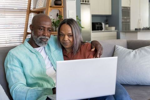 Senior african american couple relaxing on sofa and browsing laptop together at home