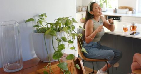 Multicultural women laughing and chatting at sunlit kitchen island with pothos and tea