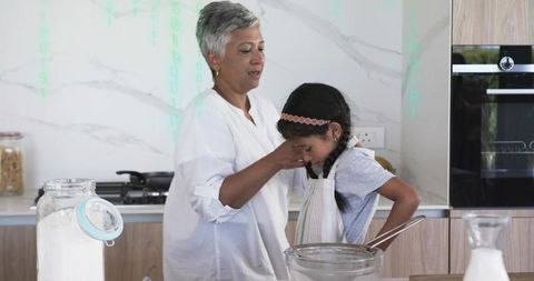 Older woman teaching young girl baking in modern kitchen, sharing warm family bonding