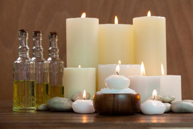 Candles with massage oil bottles and sea salt in wooden bowl on table
