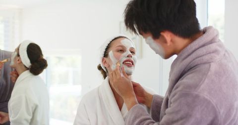 Young couple applying facial masks in bright bathroom enjoying relaxing at-home spa