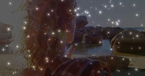 Woman dreamily gazing at rocky shoreline with magical sparkles