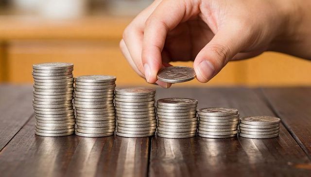 Hand adding coin to stacked silver coins showing saving growth and personal finance progress