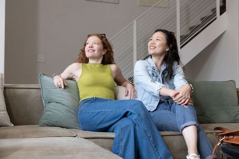Diverse female friends relaxing on sofa at home smiling in cozy living room