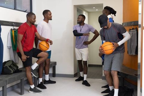 Coach leading african american basketball team in locker room huddle for motivation