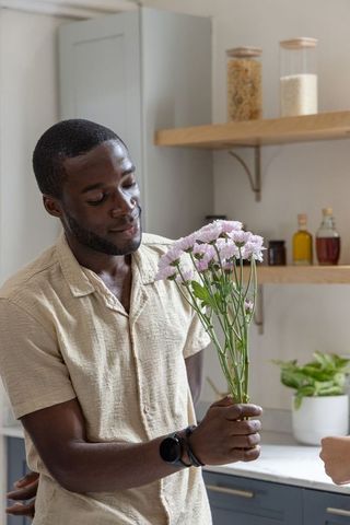 African american man holding pale pink bouquet in bright modern kitchen lifestyle