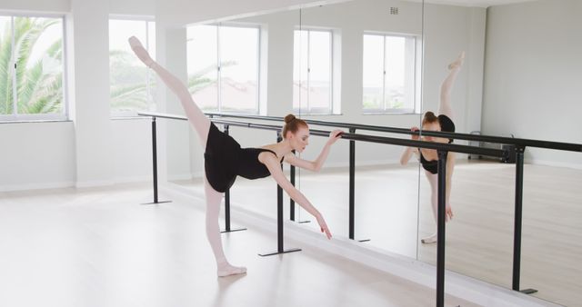 Focused caucasian female ballet dancer with leg in the air holding barre at dance studio, copy space. Dance, ballet, discipline, practice and training, unaltered.