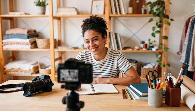 Smiling content creator filming diy tutorial in cozy home studio with dslr on tripod