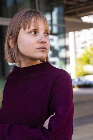Young woman looking right near modern glass facade wearing maroon sweater urban portrait