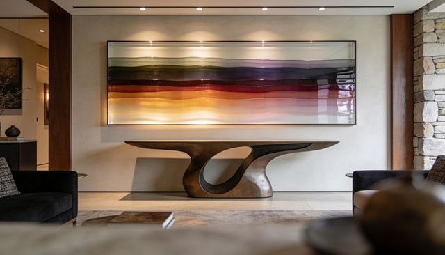 Sculptural bronze console featuring looped base and backlit abstract artwork in contemporary foyer