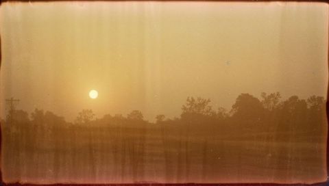 Amber sunrise over rural field with vintage film border and tree silhouettes