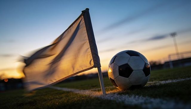 Sunset corner kick scene with soccer ball resting by fluttering flag on grassy pitch