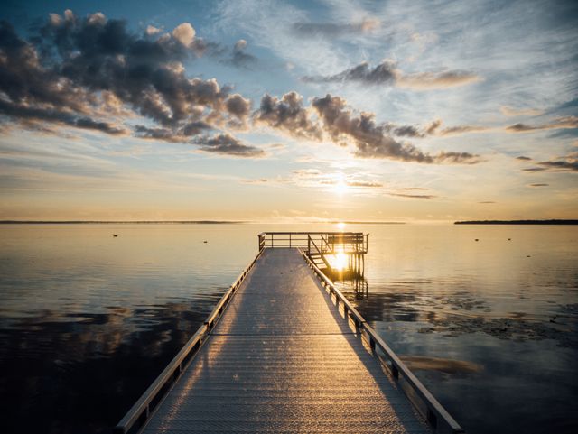 Dock extending into tranquil lake during sunset with picturesque sky and serene water reflection creates peaceful and calming atmosphere. Ideal for promoting relaxation, travel, outdoor activities, or scenic nature photography.