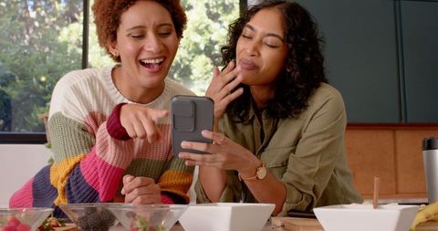 Diverse Female Friends Enjoying Casual Time with Smartphone in Cozy Kitchen