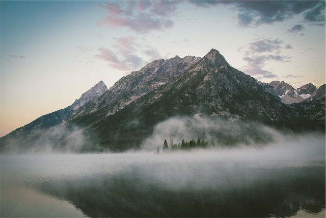Capturing a serene morning with a foggy mountain reflecting on a calm lake during sunrise. Ideal for nature, travel, and meditation content to evoke a sense of peace and tranquility. Excellent for use in inspirational social media posts, wallpapers, and background images for websites promoting relaxation and scenic beauty.