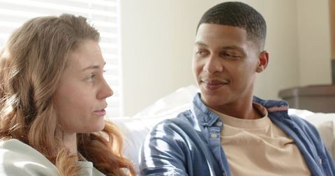 Mixed-race couple having intimate conversation on sunlit sofa, relaxed casual connection
