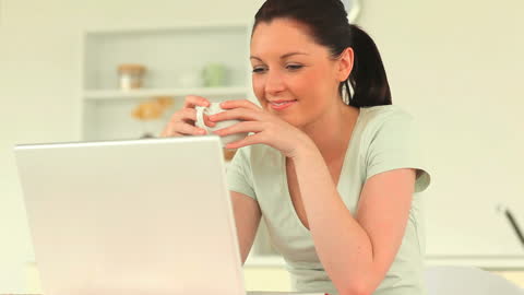 Woman Enjoying Coffee While Using Laptop in Kitchen