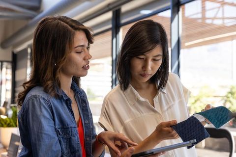 Diverse female team exploring fabric swatches with tablet technology