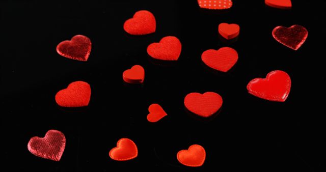Red heart-shaped objects are scattered across a dark background, with copy space. Their varying sizes and textures suggest a theme of love and celebration, for a romantic occasion like Valentine's Day.