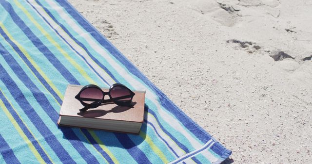 Image of sunglasses, book, towels and beach equipment lying on beach. Holidays, vacations, relax and beach concept.