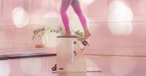 Balancing on pilates chair pressing pedal with one foot in sunlit studio