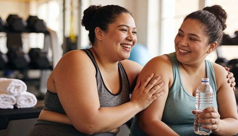 Smiling women sharing support post-workout in bright gym, hydrating together