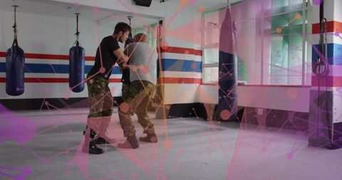 Sparring instructor guiding student through close combat grappling in camo and boots