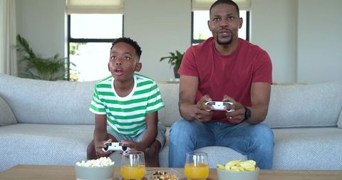 African American father and son playing video games on sofa sharing focused bonding