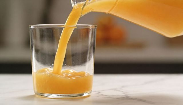 Pouring fresh orange juice into glass on marble countertop, refreshing citrus beverage