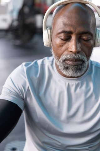 Senior african american man listening on headphones in gym, calm focused fitness portrait