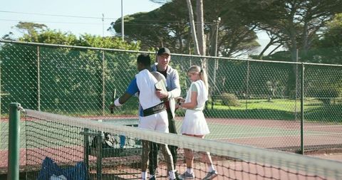 Diverse tennis team chatting with coach courtside on sunny red tennis court
