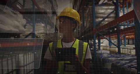 Warehouse inspector using tablet with HUD overlay wearing yellow hard hat and hi-vis vest