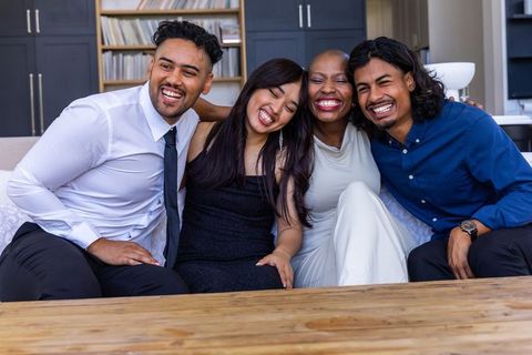 Laughing embracing multiracial friends leaning on sofa celebrating together in cozy living room
