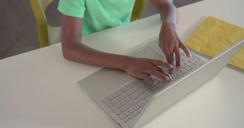African american teen typing on laptop at white desk wearing green tee, studying and concentrating