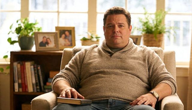 Middle-aged man relaxing in sunlit living room holding closed book