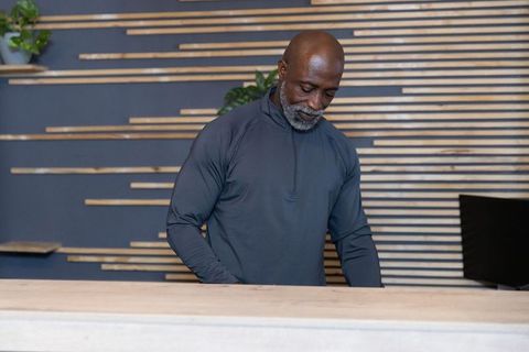 Mature male receptionist checking monitor and typing behind modern wood counter in lobby