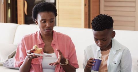 African American mother and son on couch sharing pastry and drink during serious moment
