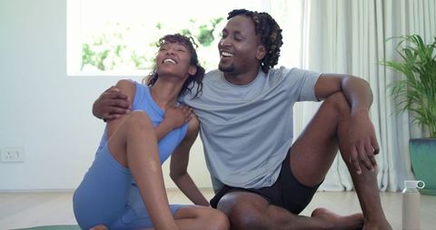 Laughing african american couple relaxing after home yoga workout in bright living room