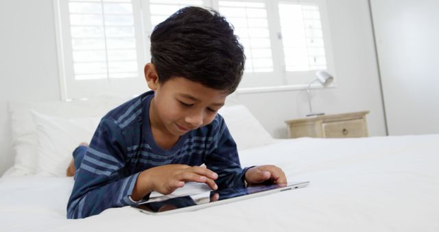Young Boy Using Tablet Device While Lying on Bed at Home - Download Free Stock Images Pikwizard.com