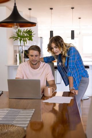 Couple collaborating on laptop at modern home dining table